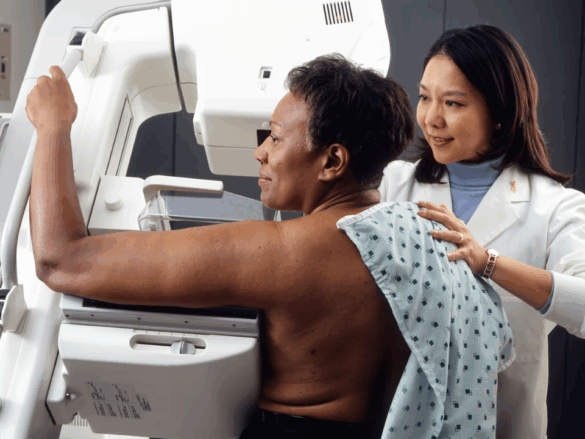 Mulher realizando exame de mamografia em ambiente hospitalar moderno, acompanhada por técnica de radiologia. Cena humanizada que representa o rastreamento e a prevenção do câncer de mama no Brasil.
