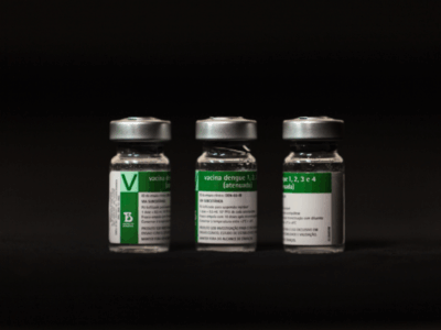 rascos da vacina Butantan-DV, imunizante brasileiro de dose única contra a dengue, alinhados sobre fundo escuro, destacando o rótulo verde do Instituto Butantan.