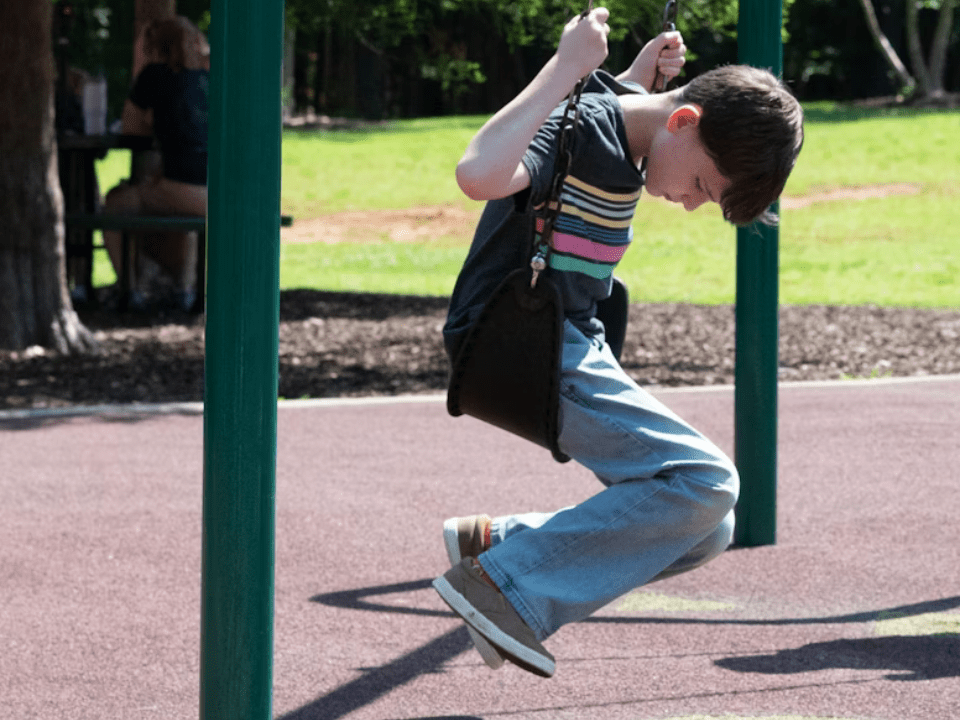 Criança sentada em balanço no parque, com postura introspectiva, simbolizando silêncio emocional e saúde mental infantil.