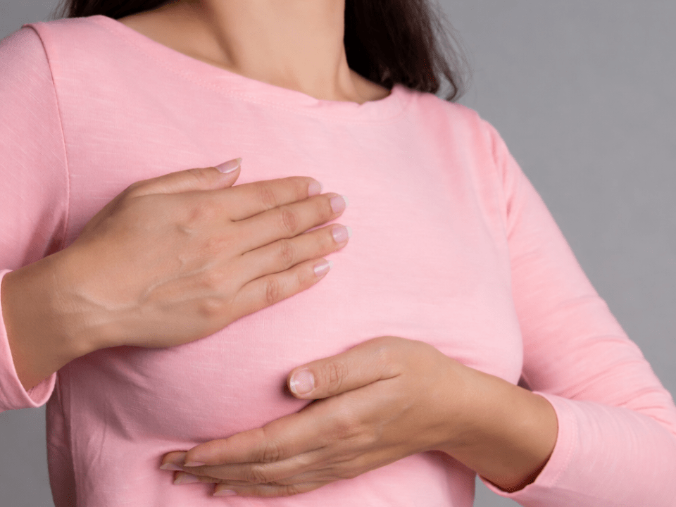 Mulher realizando autoexame das mamas, representando monitoramento e detecção do câncer de mama por métodos diagnósticos modernos.