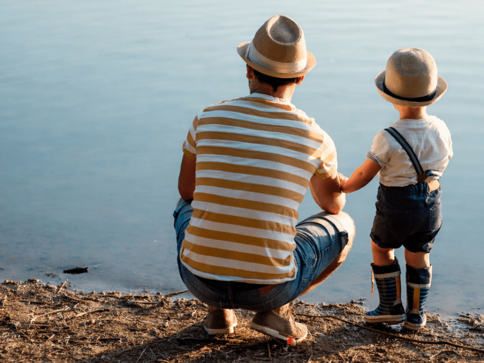 Pai e criança lado a lado à beira de um lago, representando paternidade como escola de liderança, presença e construção de caráter.