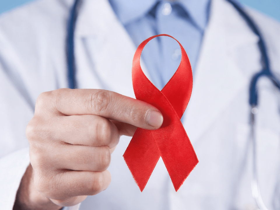 Profissional de saúde com jaleco segurando laço vermelho, símbolo de conscientização sobre HIV.