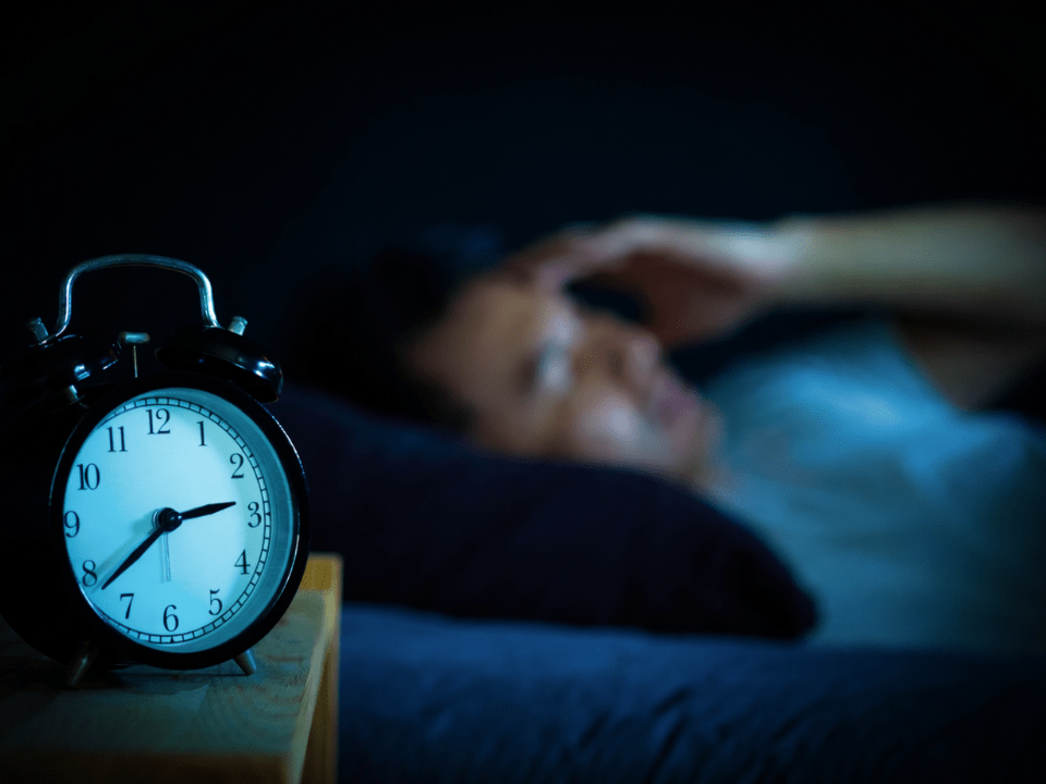 Relógio despertador marca a madrugada enquanto pessoa tenta dormir, ilustrando sono insuficiente e expectativa de vida.