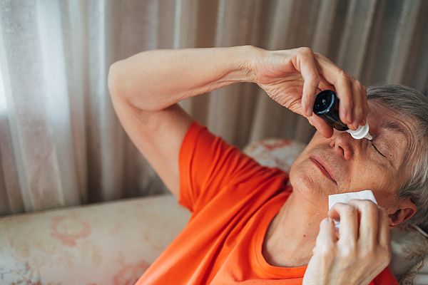 Mulher idosa aplicando colírio nos olhos em casa, relacionada ao tratamento e controle do glaucoma.