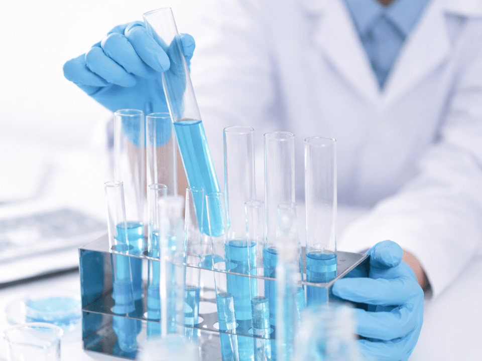 Mãos com luvas manipulando tubos de ensaio em laboratório clínico, representando o controle da qualidade da água na bioquímica clínica para garantir precisão dos resultados analíticos.