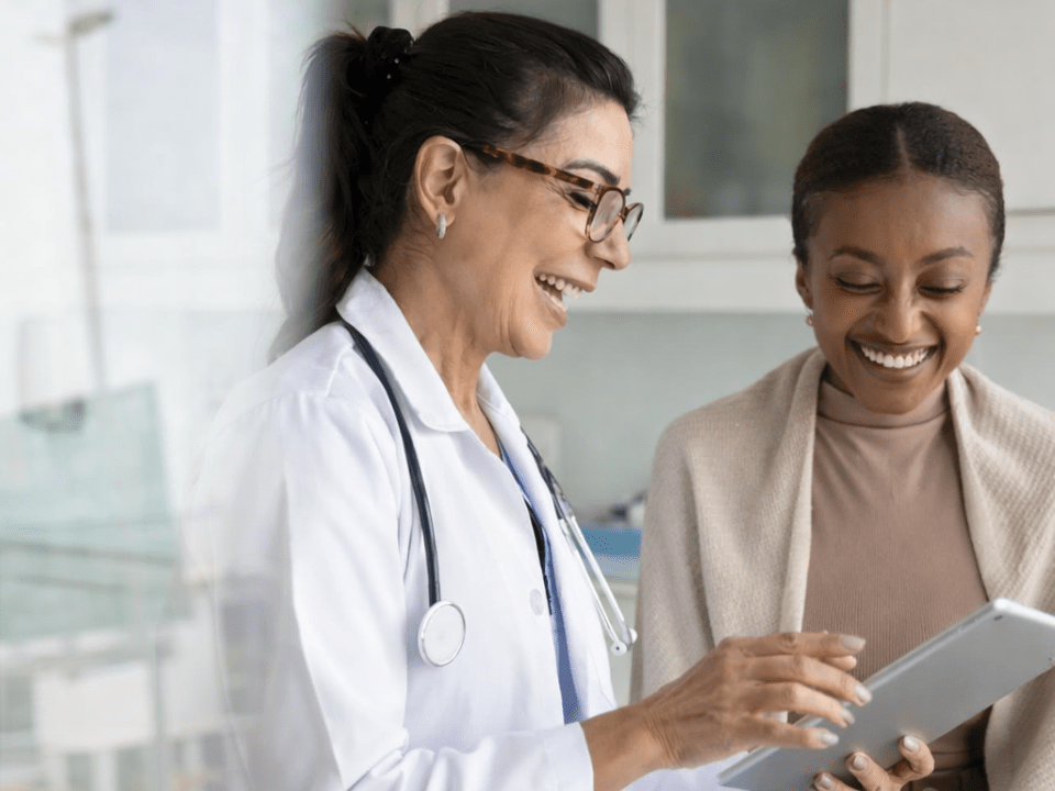 Profissional de saúde orienta paciente durante avaliação clínica com uso de tablet, ilustrando como o medo do diagnóstico evita consultas médicas e impacta negativamente o rastreamento e o diagnóstico precoce de doenças.