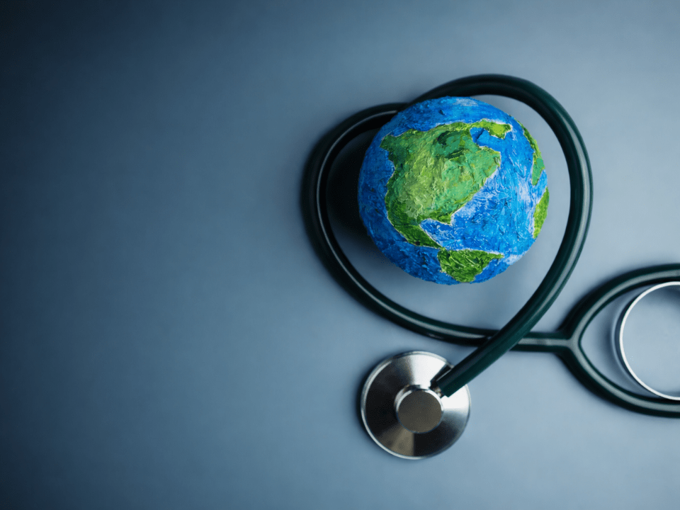 Globo terrestre envolvido por um estetoscópio em fundo azul, representando o Dia Mundial da Saúde 2026 e a integração entre ciência, medicina diagnóstica e saúde global baseada em evidências.