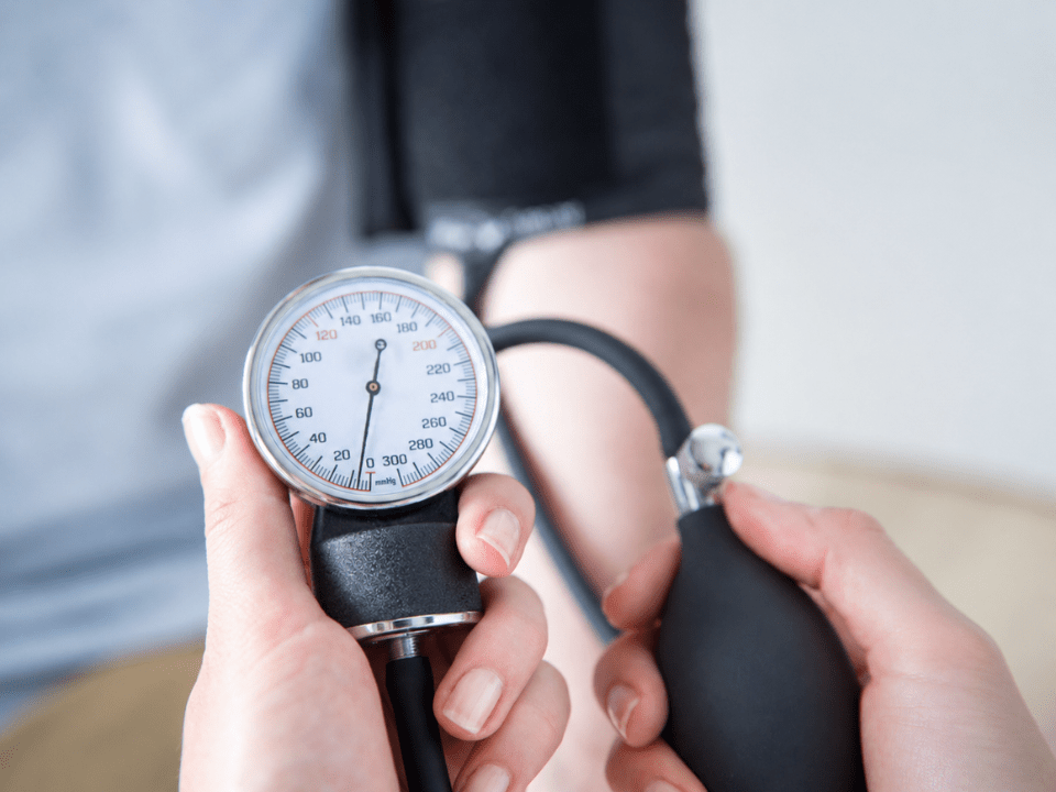 Imagem de aferição da pressão arterial com esfigmomanômetro analógico em ambiente clínico, destacando o monitoramento da hipertensão arterial e a importância do diagnóstico precoce e controle cardiovascular.