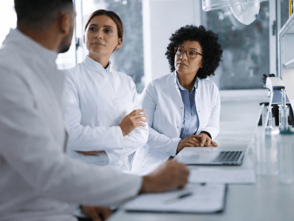 Profissionais de saúde em ambiente laboratorial discutindo dados clínicos, representando a reforma tributária em clínicas e laboratórios e a necessidade de consistência e rastreabilidade das informações em 2026.