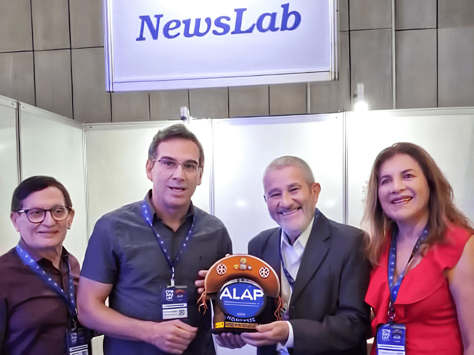Estande da NewsLab no CONGRALAP 2026 em Fortaleza, com equipe reunida e registro do encerramento do evento, incluindo a entrega de lembrança típica nordestina ao gestor comercial da revista, simbolizando a participação ativa da NewsLab no CONGRALAP 2026, com foco em análises clínicas, networking e divulgação científica no setor laboratorial brasileiro.