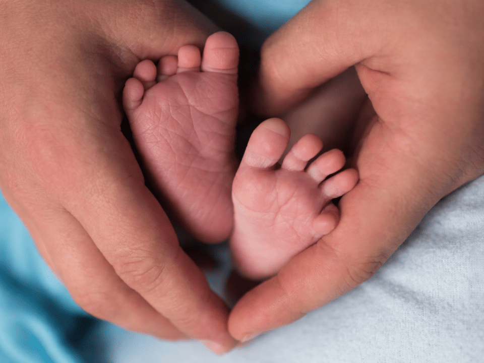 Pés de recém-nascido sendo delicadamente segurados por mãos adultas, imagem associada ao diagnóstico precoce da fenilcetonúria e ao teste do pezinho.