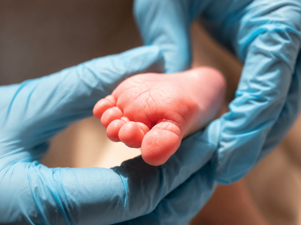 Profissional de saúde segura o pé de um recém-nascido durante procedimento relacionado ao teste do pezinho no Brasil, destacando a importância da triagem neonatal para o diagnóstico precoce de doenças graves.