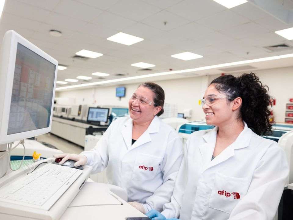 Especialistas da AFIP trabalham em ambiente laboratorial de alta tecnologia, monitorando análises e processos diagnósticos. A fotografia representa a cultura organizacional na medicina diagnóstica, evidenciando integração entre profissionais, capacitação contínua, liderança, gestão de pessoas e compromisso com a qualidade dos serviços de saúde e medicina laboratorial.