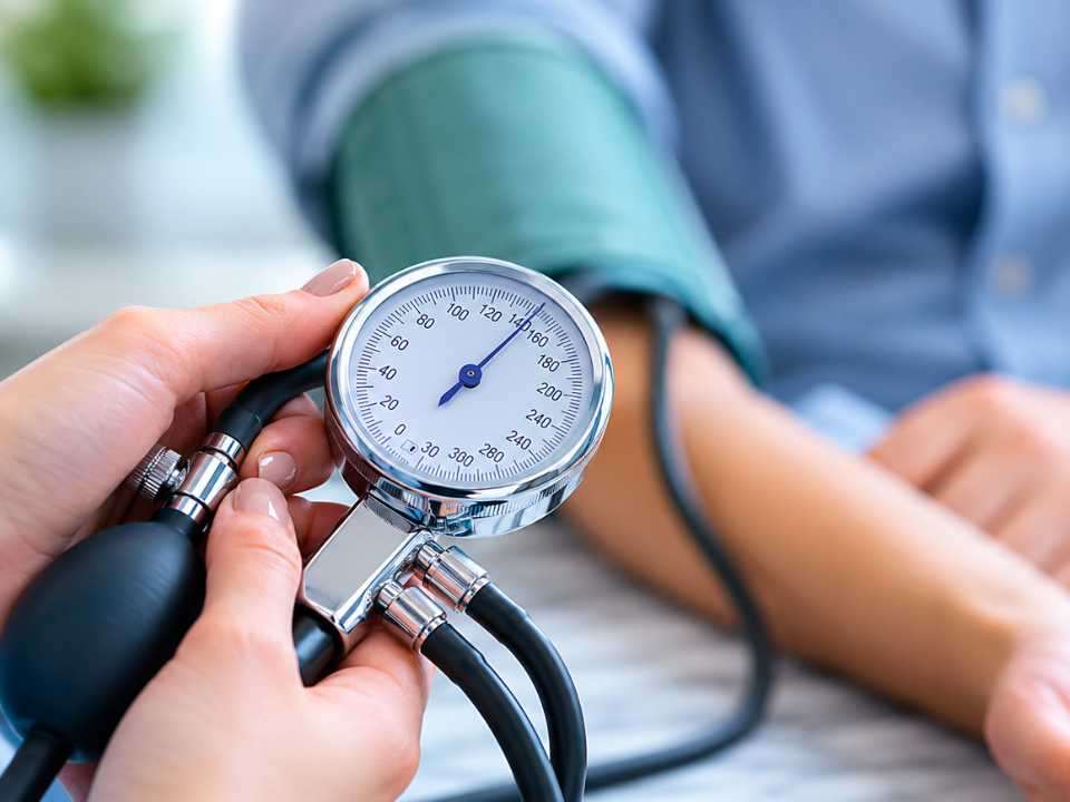 Profissional de saúde realiza aferição da pressão arterial utilizando esfigmomanômetro analógico durante atendimento clínico. A imagem ilustra o tema do webinar sobre hipertensão arterial promovido pela SBC, com foco em diagnóstico, monitoramento da pressão alta e prevenção do risco cardiovascular.