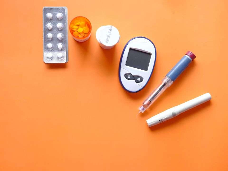 Imagem conceitual sobre diabetes em 2026, com glicosímetro, medicamentos orais, caneta de insulina e caneta de terapia injetável sobre fundo laranja, representando monitoramento glicêmico, tratamento contínuo e cuidado metabólico.