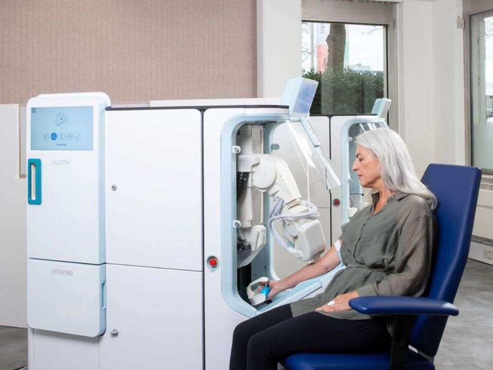 Paciente adulta com o braço posicionado no sistema robótico Aletta para coleta automatizada de sangue.