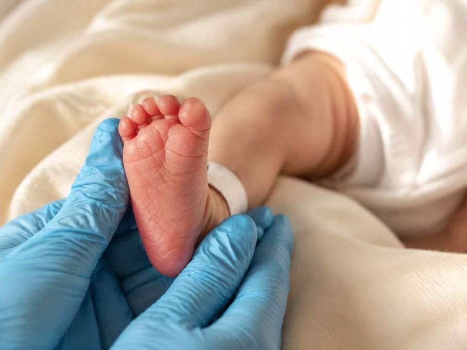 Profissional de saúde segura o pé de um recém-nascido durante procedimento relacionado à triagem neonatal.